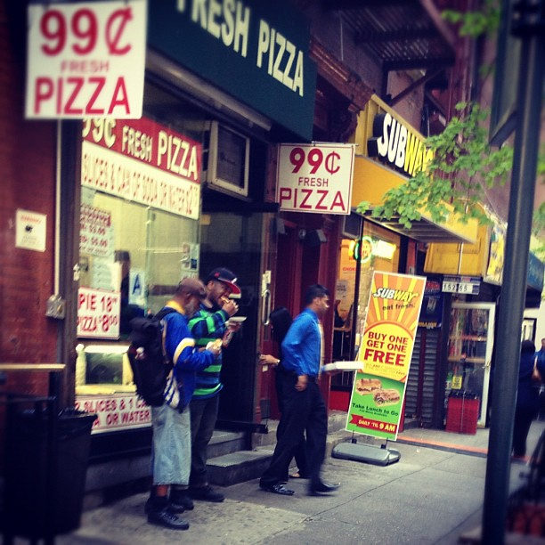 A group of people standing outside of a 99 cents fresh pizza restaurant