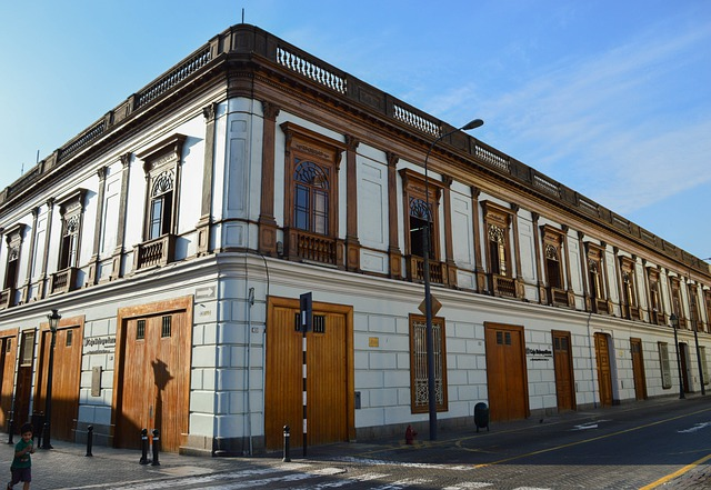 A large white building with wooden doors is on the corner of a street in Lima