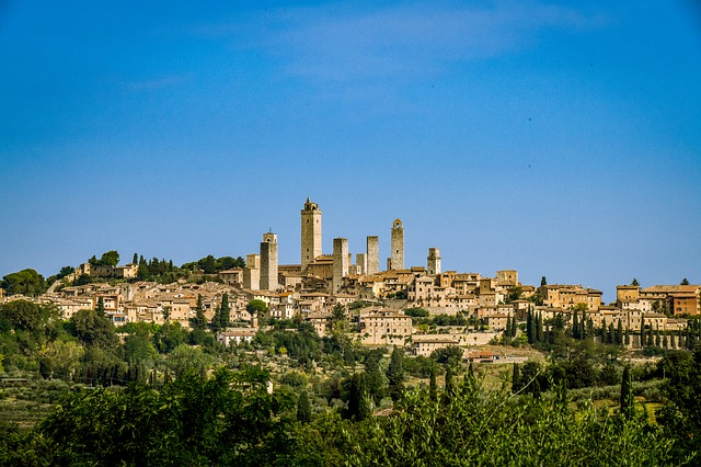A small Tuscany town sitting on top of a hill with a blue sky in the background.