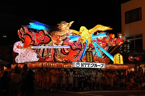 A group of people are standing in front of a large lighted sculpture in Amori City