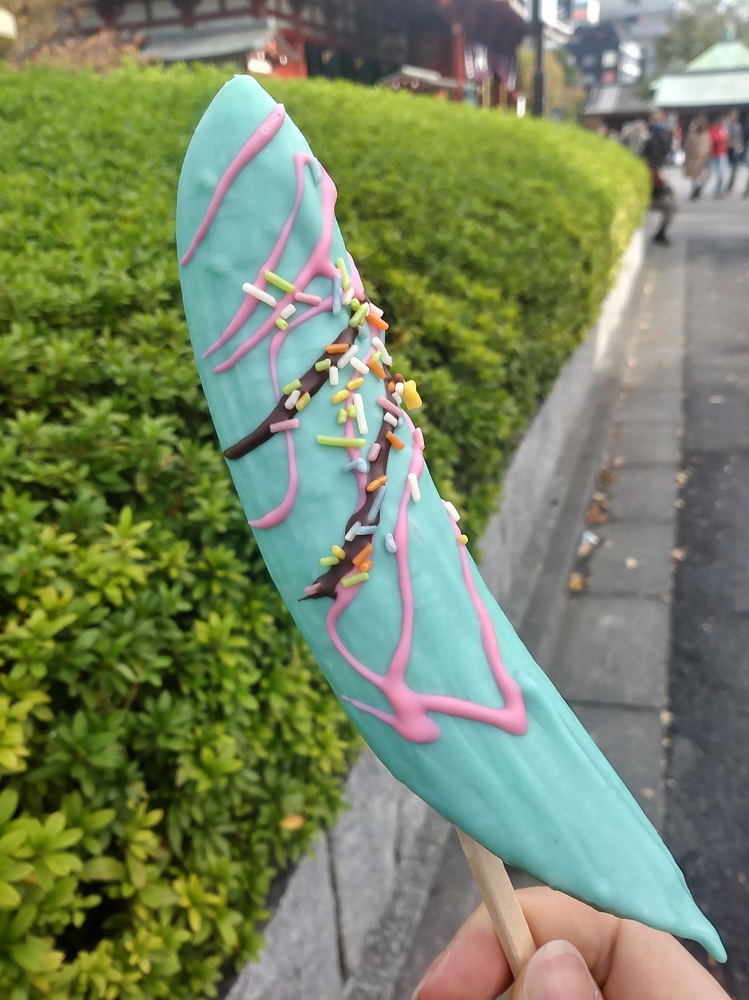 A person is holding a blue and pink chocobanana on a stick