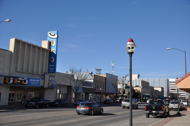 Cars are driving down a street in roswell in front of a building that says ufo