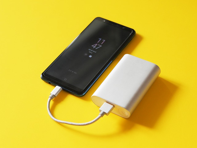 A cell phone is plugged into a power bank on a yellow background.