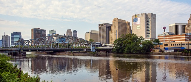 the newark skyline is reflected in the water of a river.
