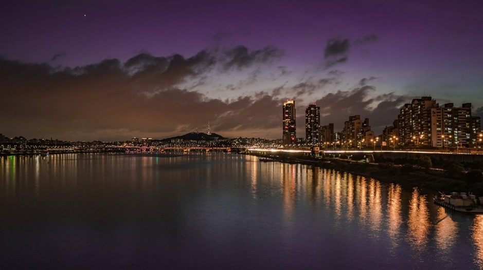 The Seoul skyline at night with a bridge over a body of water.