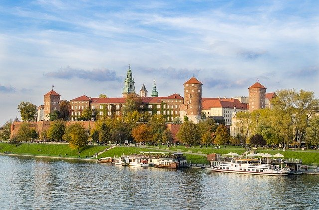 A large building is sitting on the shore of a river in Krakow