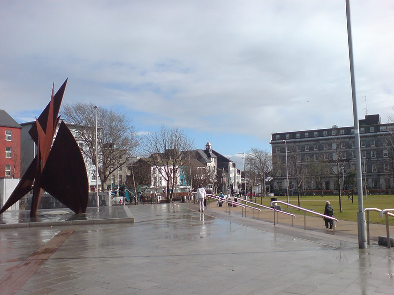 A statue in the middle of Eyre Square in Galway with buildings in the background