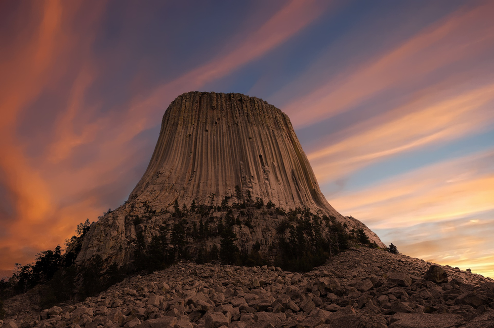 Devils tower rock formation in the desert at sunset.