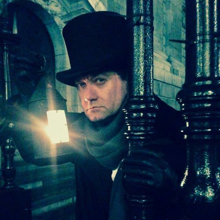 A man in a top hat is holding a lantern, preparing to host a Jack The Ripper tour 
