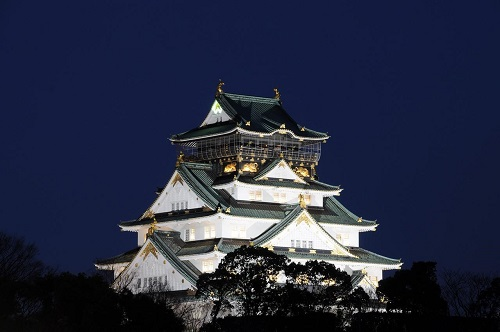 Osaka castle is lit up at night against a dark blue sky.