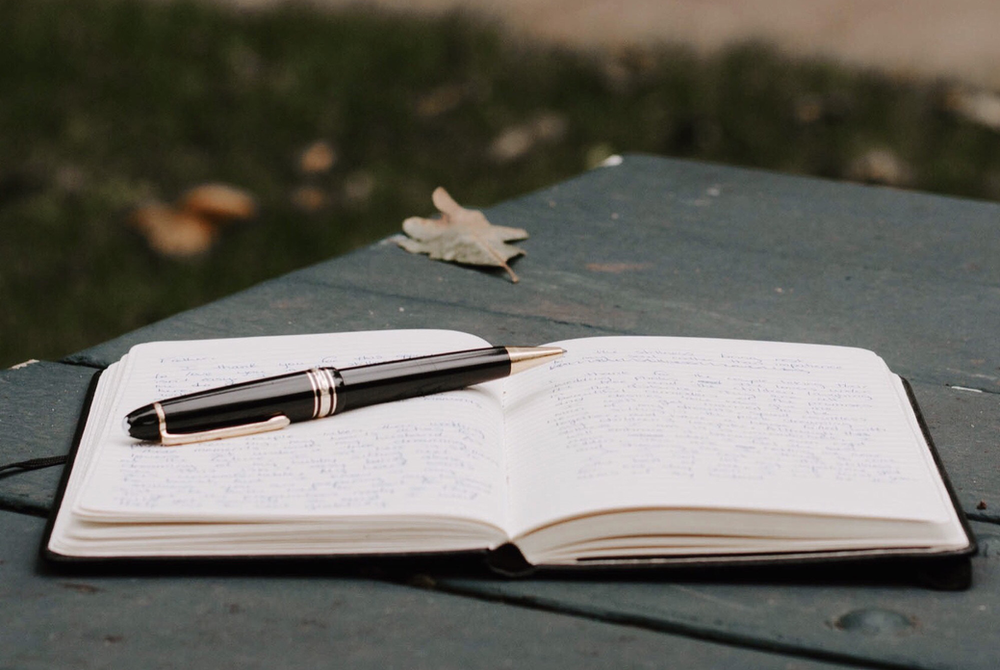 A pen is sitting on top of an open notebook on a table.
