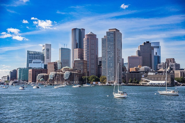 The boston skyline with boats in the water in front of it.