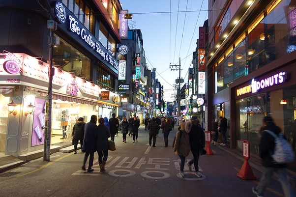 A group of people are walking down a street in front of a donut shop in Seoul.