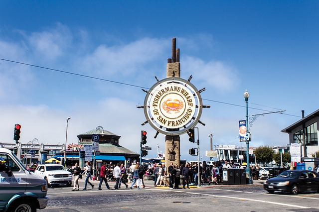 A group of people are crossing a street in front of a sign that says ' fisherman 's wharf '