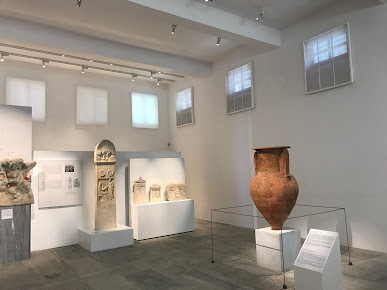 the archaeological museum of mykonos with a lot of sculptures and vases on display.