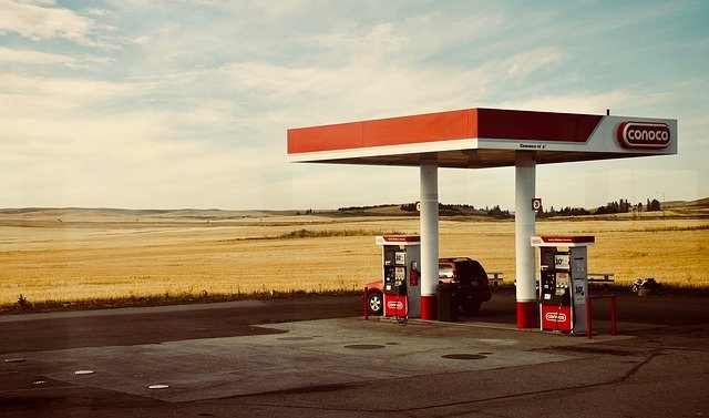 A car is parked at a gas station in the middle of a field.