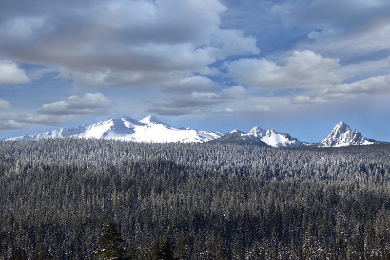 A snowy mountain range with trees in the foreground in Klamath National Forest