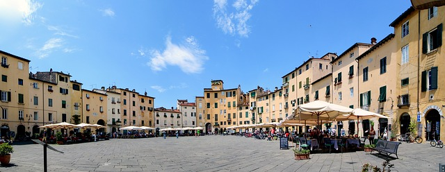A large square surrounded by buildings and umbrellas on a sunny day in Tuscany.