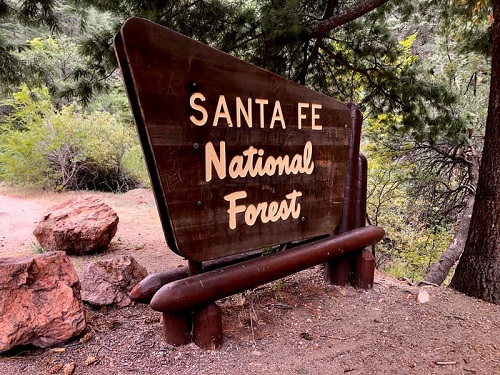 A wooden sign for santa fe national forest is sitting on top of a dirt hill.