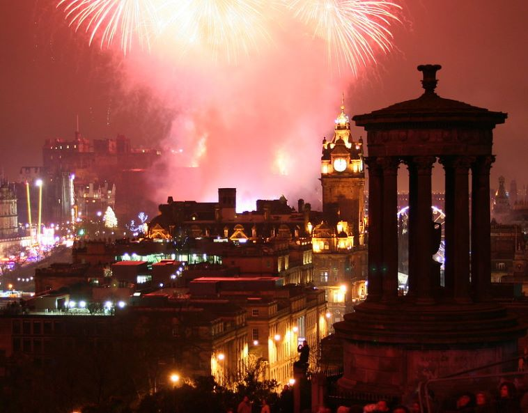 A fireworks display over a city with a statue in the foreground
