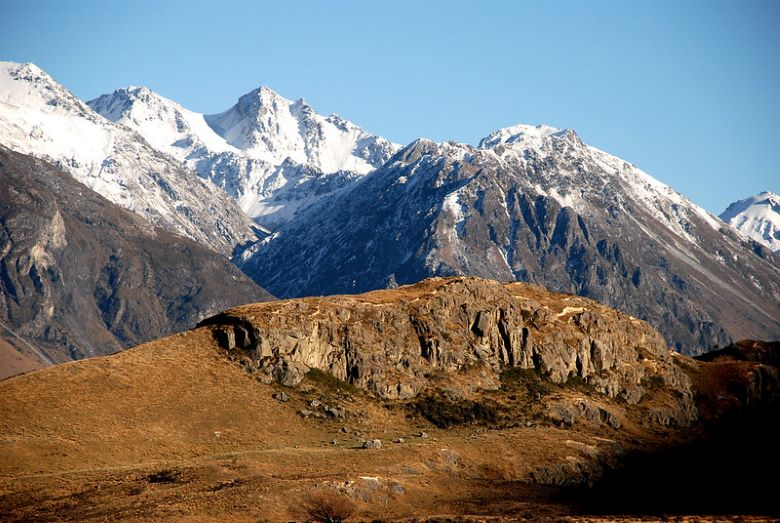 A snowy mountain range with a rocky hill in the foreground