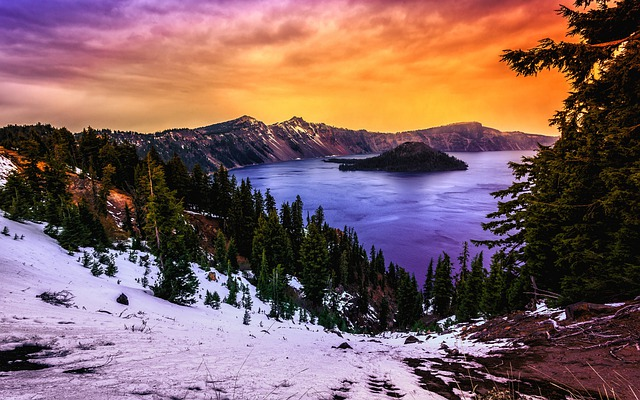 A lake surrounded by snow covered trees and mountains at sunset in crater lake np