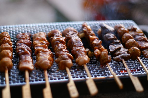 A bunch of yakitori skewers are cooking on a grill.