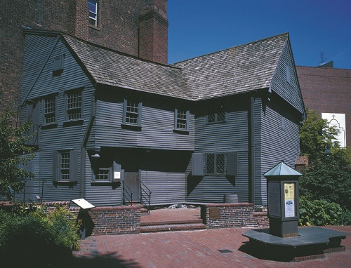 A historic black house with a brick building in the background in Boston