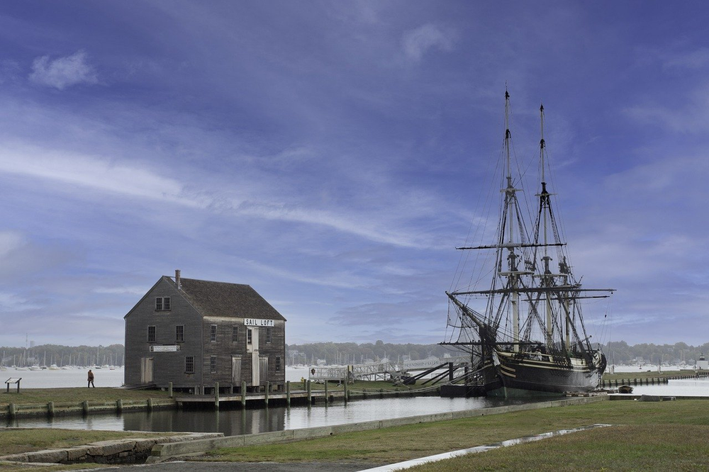 A large ship is docked next to a small house at the Salem Maritime National Historic Site