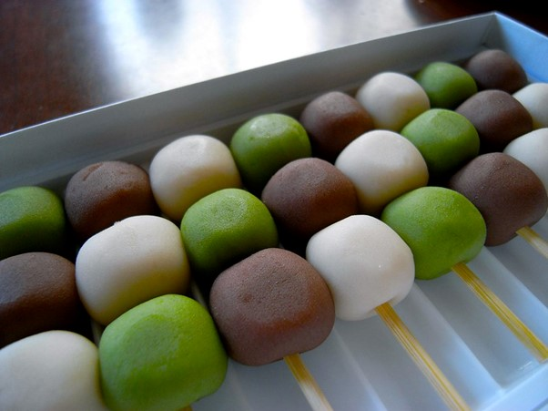 A box filled with green white and brown balls on sticks, known as dango