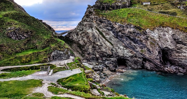 A cliff overlooking a body of water in Tintagel surrounded by mountains and grass.