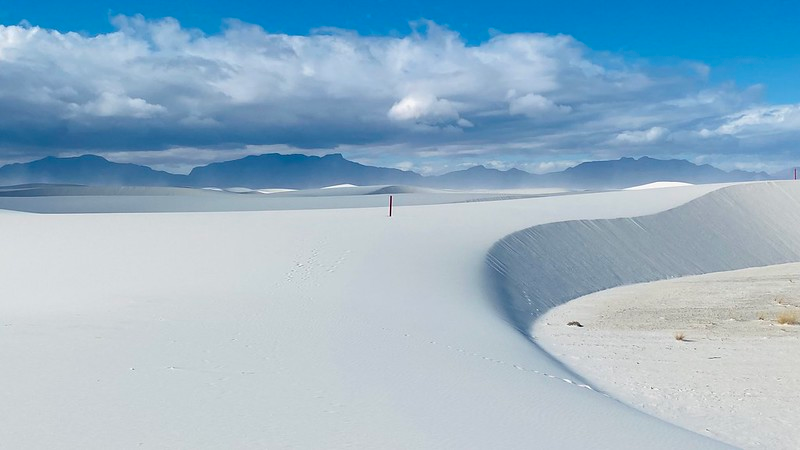 A desert in White Sands NP with mountains in the background and a blue sky with clouds