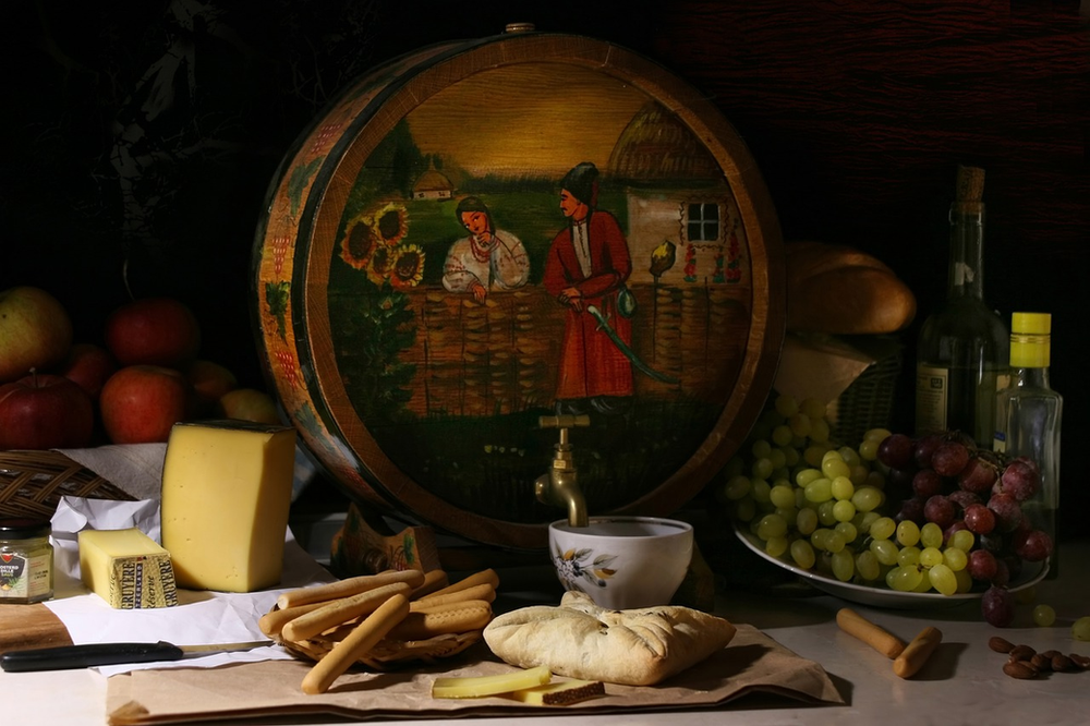 A wooden barrel with a painting on it sits on a table surrounded by food