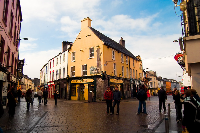 A group of people are walking down a Galway street in front of a yellow building