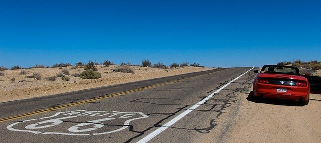 A red convertible is parked on the side of a desert road marked Route 66