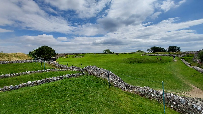 A stone wall at old sarum surrounds a grassy field on a sunny day.