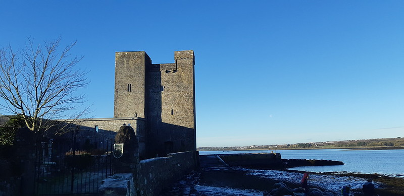 Oranmore Castle is sitting next to a body of water on a sunny day.