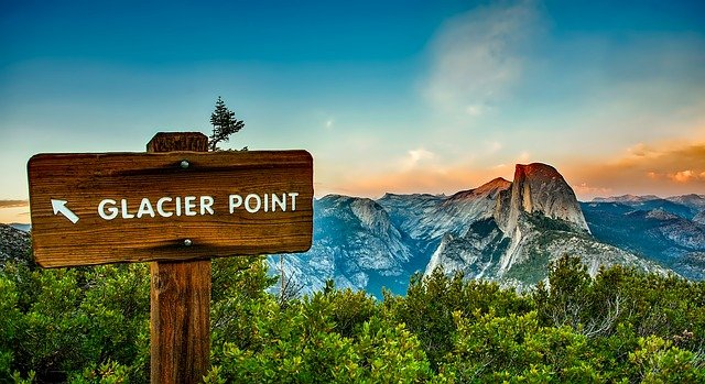 A wooden sign in yosemite np pointing to glacier point in the mountains.
