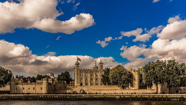 A castle in London surrounded by trees and a body of water on a cloudy day.