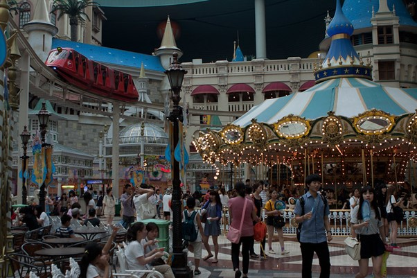 A group of people are standing around a carousel in the Lotte World amusement park.