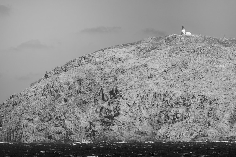 A black and white photo of a mountain with The Armenistis Lighthouse on top of it.