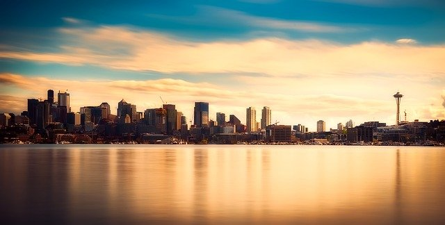 The skyline of seattle is reflected in the water at sunset.