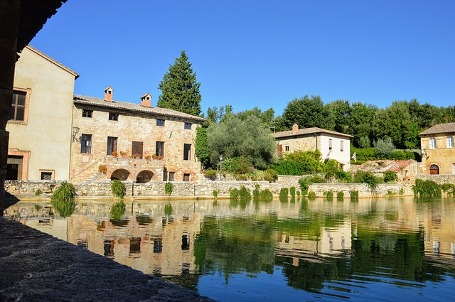 A Tuscany lake surrounded by buildings and trees with a blue sky in the background