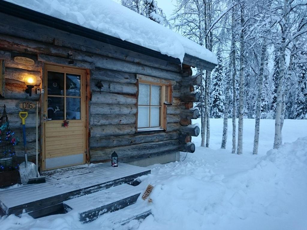 A log cabin in Lapland covered in snow in the middle of a snowy forest.