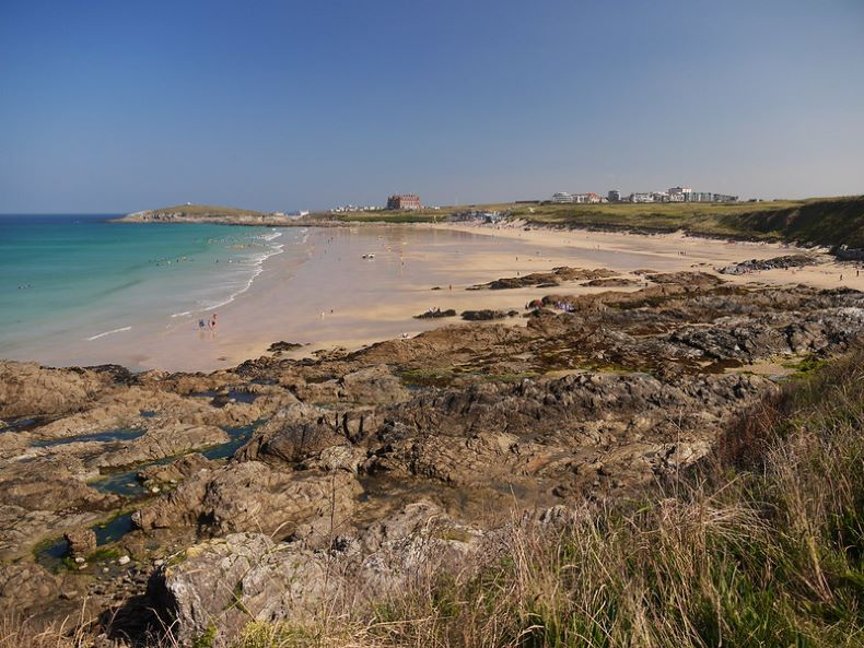 A beach in Newquay with a lot of rocks and grass on the shore