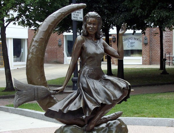 A statue of Elizabeth Montgomery sitting on a broom next to a crescent moon like she did in the tv show bewitched