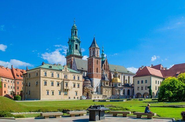 A woman is sitting on a bench in front of a large building in Krakow
