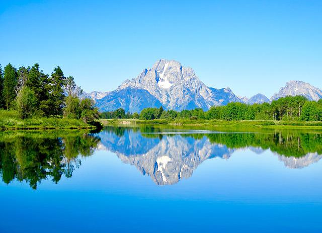 A lake with the teton mountains in the background and trees on the shore in grand teton np