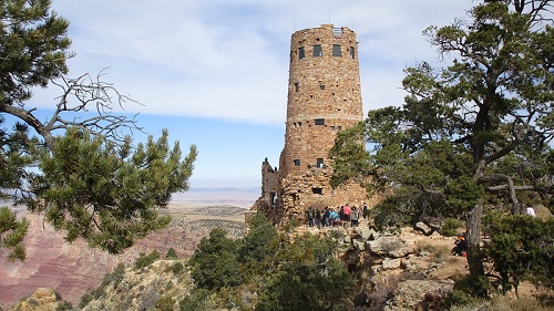 A group of people are standing in front of a tower on top of a hill at the desert view visitor center