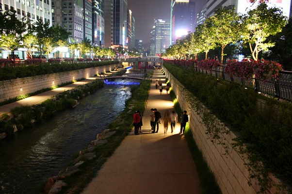 A group of people are walking along Cheonggyecheon stream in seoul at night.
